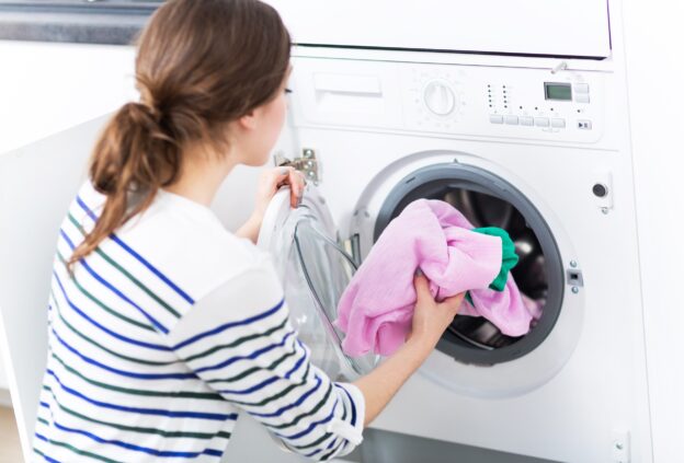 A woman loading clothes into a front-load dryer, ensuring proper dryer duct maintenance for efficient and safe drying.